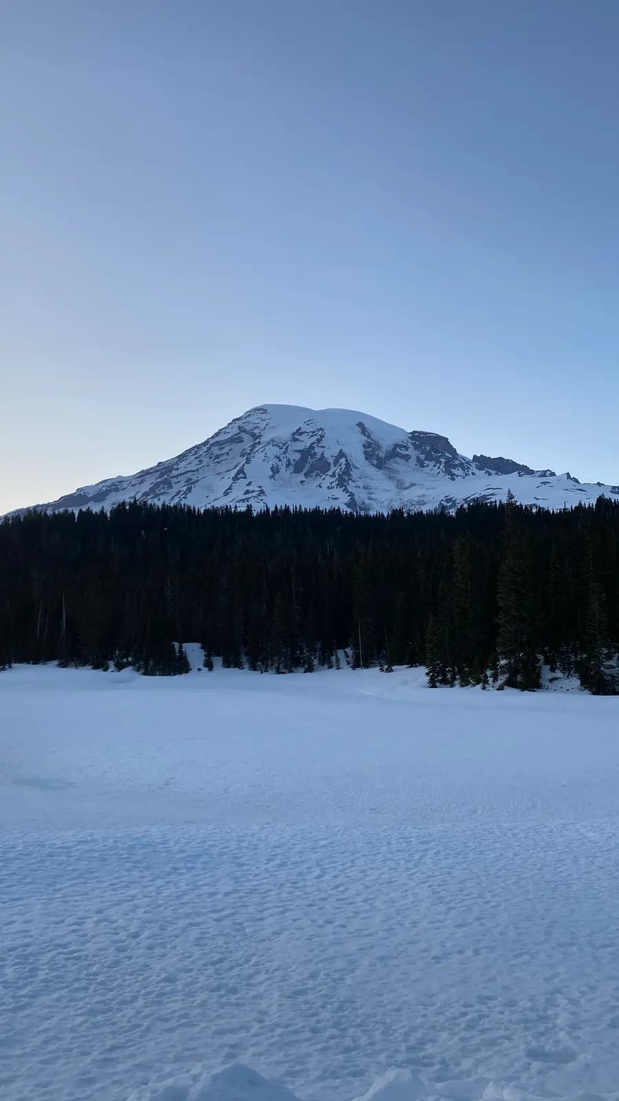Mount Rainier rising above forest and a frozen lake, seen from a campground road in the national park Mount Rainier rising above forest and a frozen lake, seen from a campground road in the national park
