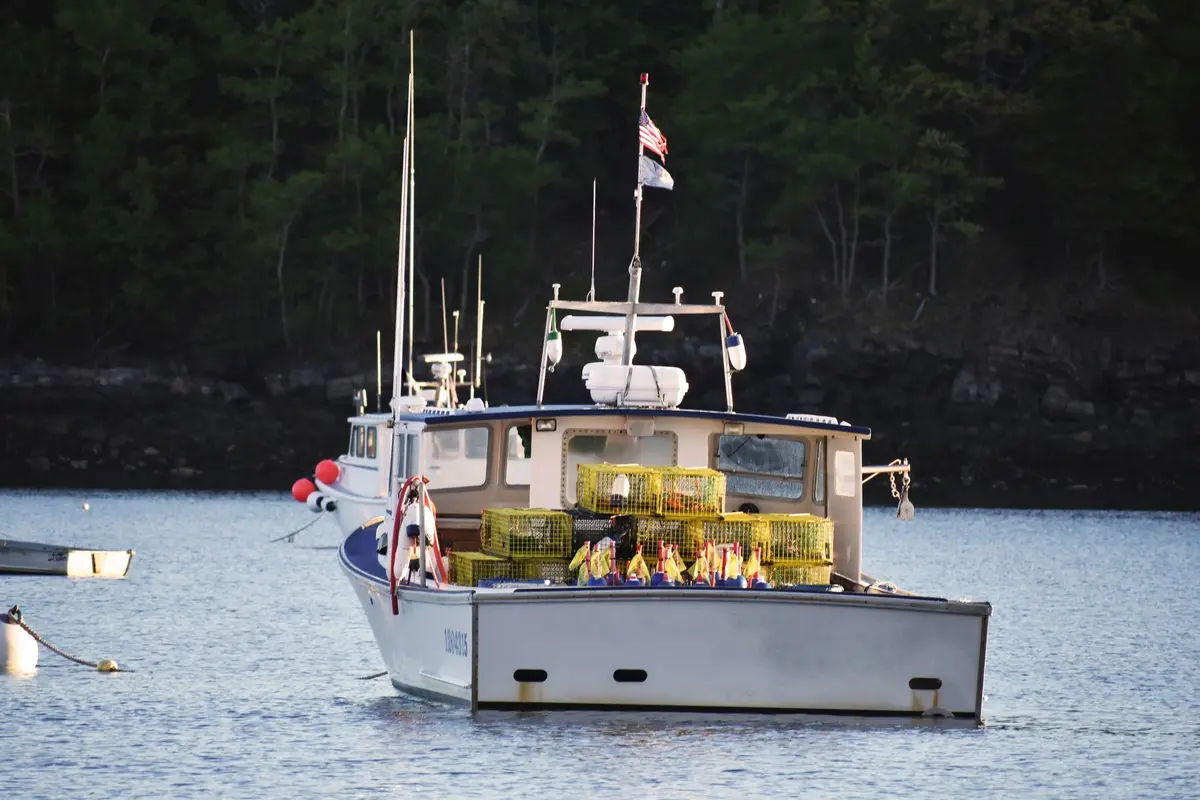 A Maine lobster boat on its mooring with yellow traps and buoys stacked on the stern