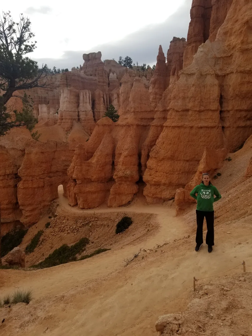 A hiker on the sandy trail between tall orange hoodoos in Bryce Canyon