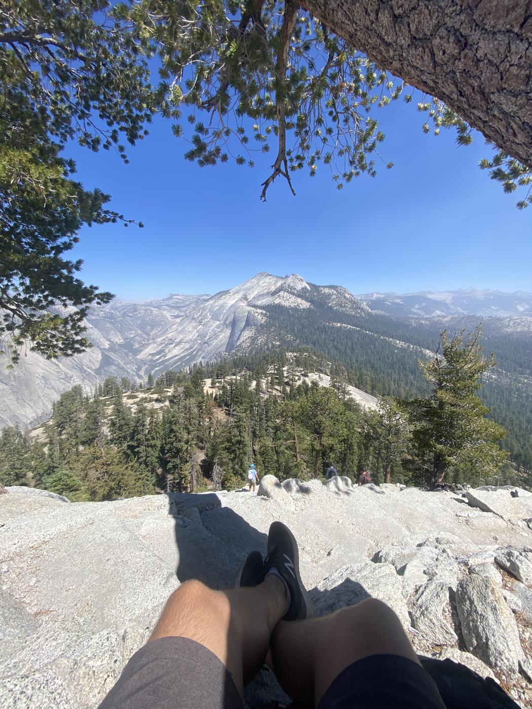 A hiker resting on open granite with the Yosemite high country and distant domes beyond