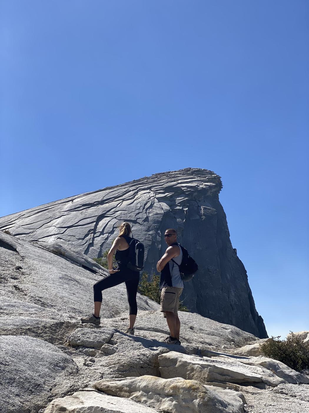 Two hikers on the Sub Dome looking up at the granite summit of Half Dome, Yosemite