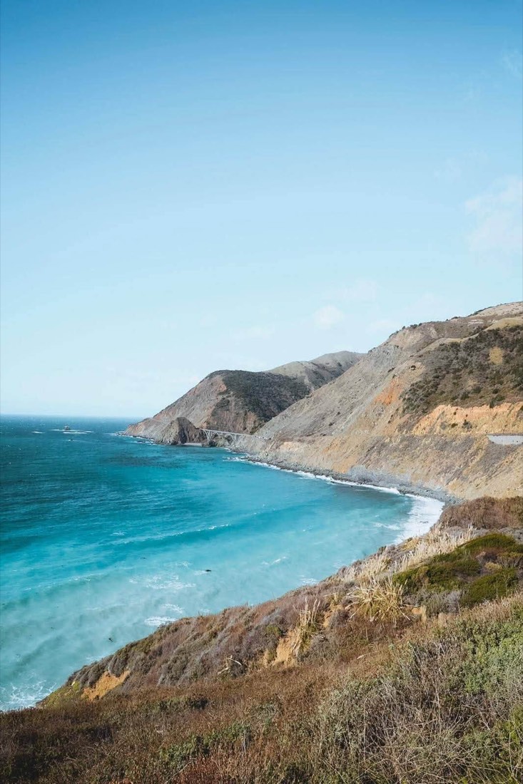 Highway 1 curving above a turquoise cove on the Big Sur coast